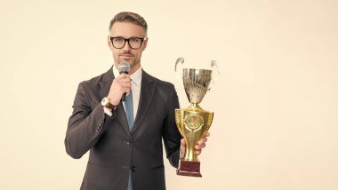 positive mature man in suit hold champion cup and microphone isolated on white background.