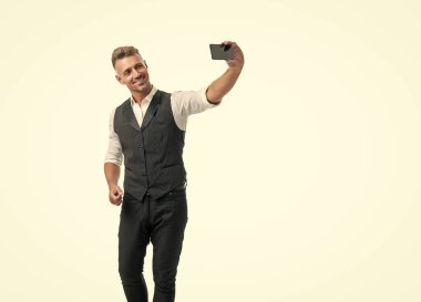 Happy professional guy in suit vest making videochat using smartphone isolated on white.