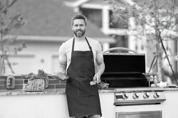 stock image positive man cook salmon outdoor. man cook salmon in apron. photo of man cook salmon food. man cook salmon on grill.