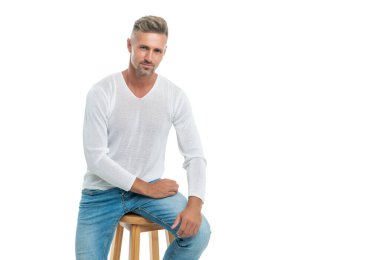 Gülümseyen, gri saçlı, olgun, beyaz arka planda izole bir şekilde oturan, erkeklerin güzelliği..