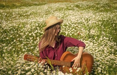 Güzel vakit geçiriyorum. Romantik ruh hali. Bahar doğasının güzelliği. Papatya çiçekleri içinde gitarlı mutlu bir kız. Yaz tatili ve tatil. Güzel bir kadın papatya tarlasında şapka takar. Çayır şarkıcısı.