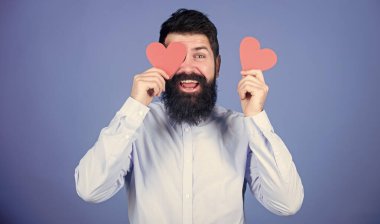 Aşk duyguların dilidir. Hippi gözlerini küçük bir kalple kapatıyor. Kırmızı kalp tutan sakallı adam. Kalp şeklinde kartları olan seksi bir sevgililer günü erkeği. Sevgililer günün kutlu olsun. Aşkın bayramı.