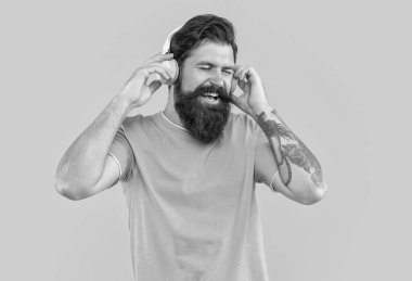 Kulaklıklı neşeli adamın stüdyo fotoğrafı. Havalı adam müzik dinler. Sakallı adam sarı arka planda izole edilmiş kulaklıkla müzik dinliyor. Adam kulaklıkla müzik dinliyor. müzik konseptini dinle.