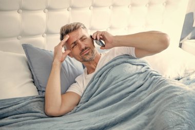 Uykulu, olgun bir adam telefonda konuşuyor. Baş ağrısı.