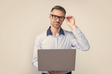 Gri arka planda bilgisayar üzerinde çalışan gözlüklü olgun bir iş adamı..