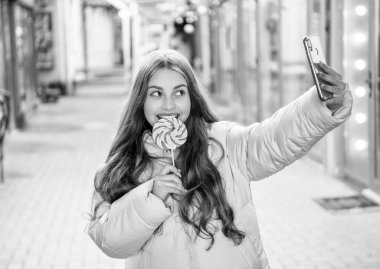 Neşeli blogcu kız şapka takarak akıllı telefon özçekimi yapıyor. Blogcu kızın dışarıda akıllı telefon özçekimi yaptığı fotoğraf. Blogcu kız lolipopla akıllı telefon özçekimi yapıyor. Blogcu kız dışarıda akıllı telefon özçekimi yapıyor..