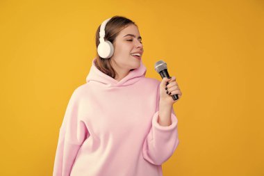 Kulaklıklı mutlu genç kız sarı arka planda mikrofonla şarkı söylüyor..