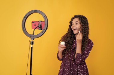 Uzun kıvırcık saçlı hayret bir çocuk blogda pudra fırçası için video çekiyor..