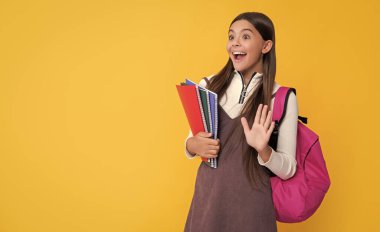 amazed child with school backpack and workbook on yellow background.