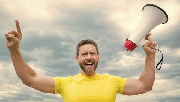 stock image man in yellow shirt shout with loudspeaker on sky background.