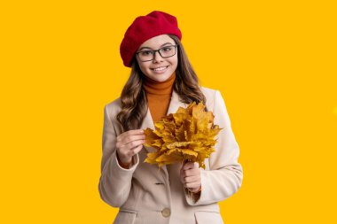 Yaprakları dökülmüş genç kız sarıda soyutlanmış. Sonbahar kızı dökülen yaprakları tutar. Sonbahar ve sonbahar. Sonbahar sezonu. Sonbahar modası. Sarı akçaağaç yapraklarını neşeyle tutan mutlu genç kız. Sonbahar yürüyüşleri.