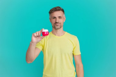 Olgun adam cilt kremi kullanır. Günlük alışkanlık ve kişisel bakım. Cilt güzelliği. Erkek güzellik kozmetiği. Erkek kozmetik ürünü sunan adam. Mavi renkte yüz kremi gösteren bir adam var. Deriyi sulandır..