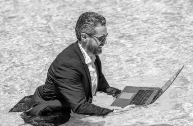 Yüzme havuzunda dizüstü bilgisayarı olan iş adamı. Yaz tatilindeki iş adamı. Yüzme havuzunda dalgıç kıyafetli bir iş adamı. Uzaktan kumanda çalışıyor. Yaz iş hayalleri. Başarılı adam. Yaz seyahati.
