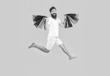 Alışveriş meraklısı mı alışveriş meraklısı mı? Adam dükkanda çantalarla zıplıyor. Alışveriş yapan adam sakallı zıplıyor. Dükkan satın alma konsepti. Alışverişkolik adam sarı arka planda izole edilmiş..