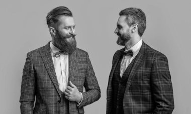 Gri arka planda izole edilmiş neşeli smokinli adamlar. Smokinli iki adam. Smokin giyen adamların stüdyo fotoğrafı. Resmi takım elbiseli şık adamlar..