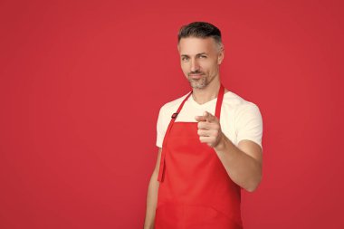 Kırmızı arka planda önlüklü olgun bir barmen. işaret parmağı.