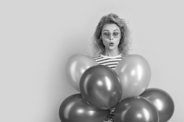 Güneş gözlüklü balonlu bir parti kadını. Şaşırmış bir kadın stüdyoda parti balonları tutuyor. Parti için balonu olan kadın sarı arka planda izole edilmiş..