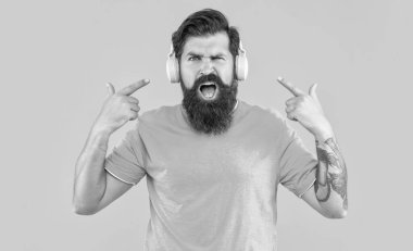 Yüksek sesli müzikten rahatsız olmuş bir adamın stüdyo çekimi. Sinirli adamın sarı kulaklıklarda yüksek sesli müziği var. Sinirli adam kulaklıkla yüksek sesle müzik dinler. Yüksek sesli kulaklıklı rahatsız bir adam.