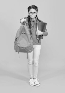 Okul çantasını sarı arka planda tutan mutsuz genç kız. Okul eğitimi. Okula geri dön..