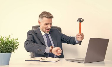 Sinirli patron çekiçle dizüstü bilgisayara vuruyor ve zamanı kontrol ediyor..