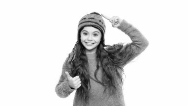 Sıcak şapka giyen genç kız beyaz arka planda izole edilmiş baş parmağını kaldırıyor. Genç kız stüdyoda süveter ve kalın bir şapka giyer. Genç kızlar için kış modası. Sıcak şapka örgüsü. Sıcak şapkalı genç kız..