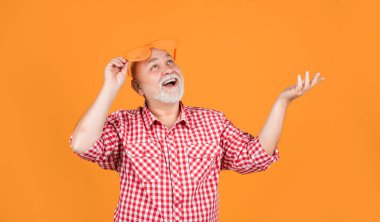 Sarı arka planda damalı gömlek ve parti gözlüğü takan yaşlı bir adam..