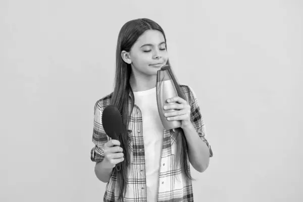 stock image teen girl do haircare and smell shampoo in studio. haircare of teen girl with hairbrush. teen girl taking care of hair with hairbrush, haircare. teen girl haircare by combing hair isolated on yellow.