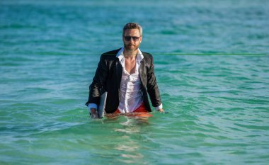 Yaz tatilindeki yakışıklı iş adamı. Denizdeki iş adamı dizüstü bilgisayarını tutuyor. Yaz işi. Yaz Denizi Sahili 'nde serbest yazar. İş adamı iş gününden sonra ferahlatıcı. iş tatili.