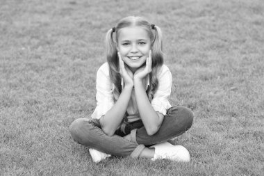 Genç kız dışarıda oturuyor. Gençliğin çocukluk tarzı. Yaz çimlerinde rahatla. Kız çimlerin üzerinde huzur içinde dinleniyor. Genç kızın mutlu çocukluğu. Yaz tatilinde parkta dinlenmek. Doğayla çevrili..