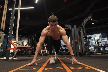 Spor salonunda çömelmiş, çömelmiş bir sporcu. Önde diz çökmüş bir sporcu ve spor salonunda başlama çizgisine uzanıyor. Spor salonunda koşmak. Egzersiz yap. Spor ve spor.
