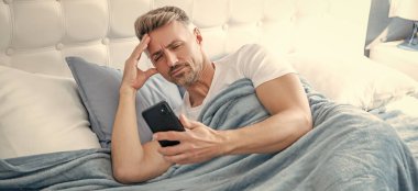 Uykulu, olgun bir adam yatakta telefonda konuşuyor..