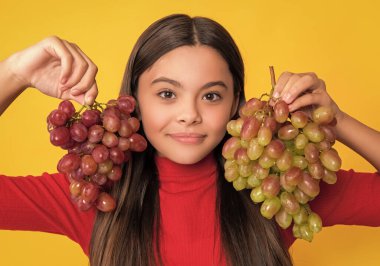 smiling teen girl hold bunch of grapes on yellow background.