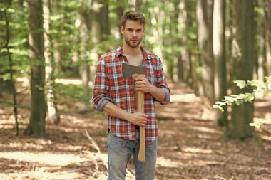 Unshaven guy in lumberjack style standing with axe forest background.