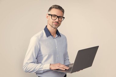 Gözlüklü olgun yönetmen gri arka planda bilgisayar üzerinde çalışıyor..