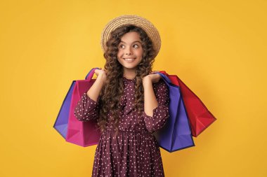 Kıvırcık saçlı pozitif kız sarı arka planda alışveriş torbaları tutuyor..