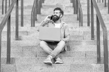 guy smile has online video communication on laptop. guy has online video communication outdoor. guy has online video communication outside. guy has online video communication sitting on stairs.