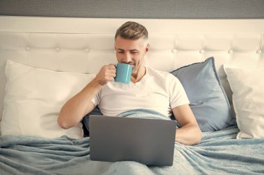 Keyifli, olgun bir adam laptopta kahveyle yatakta çalışıyor..