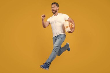 Energetic courier guy running with present box in midair yellow studio background. Courier service. Fast courier delivery.