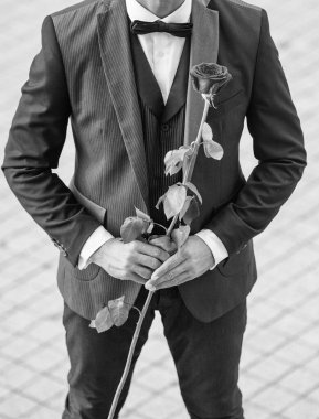 Smokinli şık bir adam. Dışarıda papyon giyen bir adam. Kırmızı güllü smokin giyen adamın kırpılmış görüntüsü..