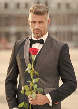 portrait of man in tuxedo at romantic occasion. man with romantic present. handsome romantic man with rose.