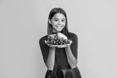 smiling girl hold fresh fruit plate on yellow background.