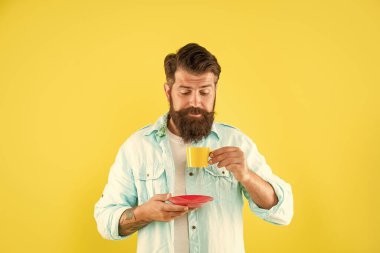 Sakallı duygusal hippi sarı arka planda kahve fincanına bakıyor, espresso..