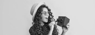 Kıvırcık saçlı hayret bir çocuk sarı arka planda hediye kutusunu tutuyor..