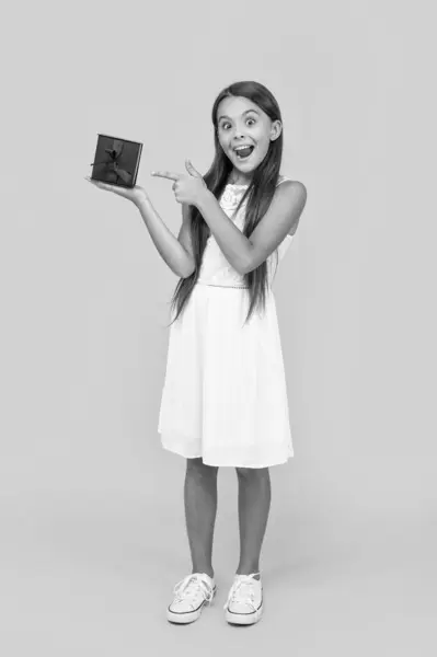 stock image amazed teen girl point finger on present box on yellow background.