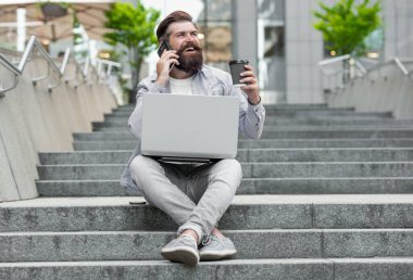 Cep telefonuyla konuşan, kahve içen mutlu bir adam. Gülümseyen adam cep telefonuyla konuşuyor. Merdivenlerde dinleniyor. Mobil iletişim. Cep telefonundan arıyorlar. Telefon görüşmesi.