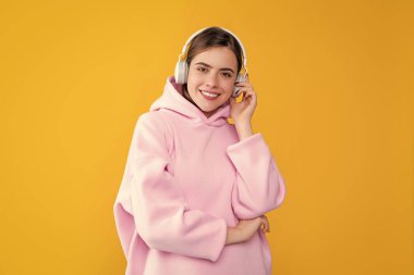 Mutlu genç kadın sarı arka planda kulaklıkla müzik dinliyor..