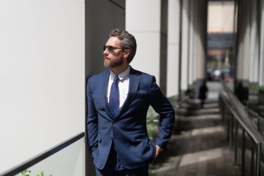 İş adamı kılığındaki başarılı hırslı işadamı modern iş bürosu binasında duruyor..