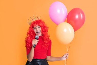 Sarı arka planda parti balonu ve mikrofonla taç takmış çocuk gülümsemesi..