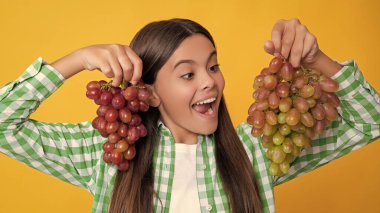 amazed teen kid with fresh grapes bunch on yellow background.