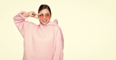 Happy girl in casual pink hoodie and glasses showing v-sign two fingers gesture isolated on white, victory.